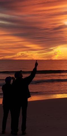 Two people gazing at sunset while walking on a beach